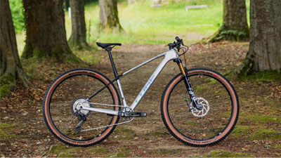 Je ziet een zilveren Cube mountainbike op een bospad.