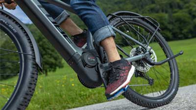Afgebeeld is een close-up van een grijze Cube Reaction Hybrid Allroad fiets. Tijdens de rit worden de trapas en het motorblok van de e-bike van dichtbij bekeken.