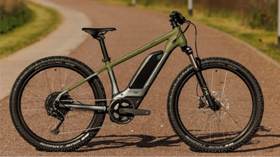 Je ziet een grijze Cube e-bike voor kinderen met groene details. Hij staat op een geasfalteerd fietspad.