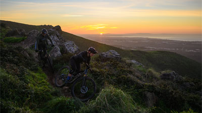 Twee fietsers rijden een berg af, elk op een Cube Stereo Fully mountainbike.