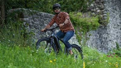 Een fietser rijdt op zijn mountainbike door een weiland met een stenen muur op de achtergrond.