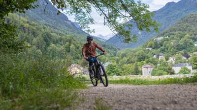 Een fietser rijdt op zijn mountainbike over een grindpad, met een berglandschap op de achtergrond.