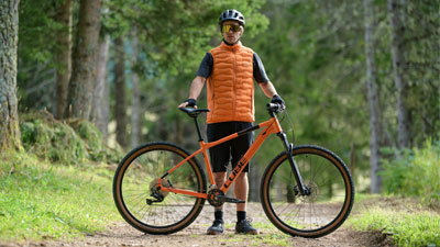 Een man staat achter zijn oranje Cube mountainbike op een bospad.
