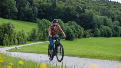 Een fietser rijdt op zijn mountainbike over een geasfalteerd fietspad, met een landelijk landschap op de achtergrond.