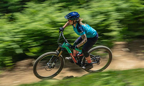 Je ziet een vrouw op een mountainbike snel over een bospad rijden.