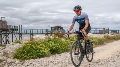 Je ziet een man in fietskleding. Hij rijdt op zijn gravelfiets op een strandpad.