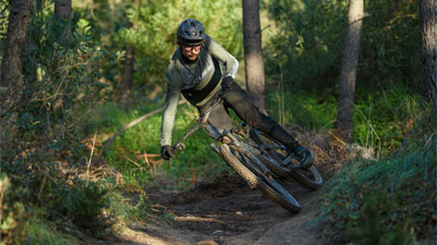 Fietser rijdt diagonaal door het bos op een Cube Stereo Fully mountainbike.