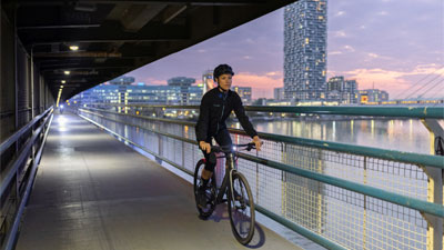 Je ziet een vrouw op haar fiets, ze rijdt door een metro, op de achtergrond zie je een grote stad.