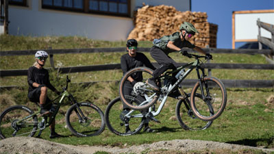 Een kind springt op een Cube Stereo Fully mountainbike, twee fietsers kijken toe.
