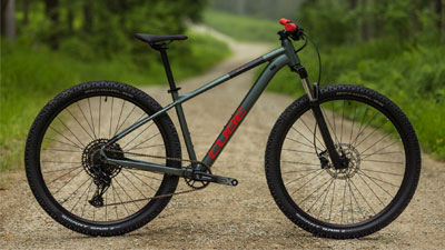 Je ziet een grijze Cube mountainbike met rode details op een grindpad.