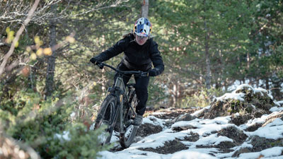 Een fietser rijdt op haar mountainbike door het oneffen bos, de grond is hier en daar nog bedekt met sneeuw.