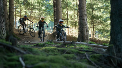 Twee tieners en een fietser rijden door het bos op Cube Stereo Fully mountainbikes.