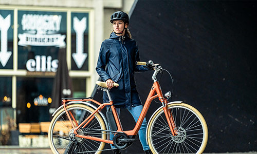 Een vrouw staat achter haar oranje stadsfiets in het centrum van de stad.