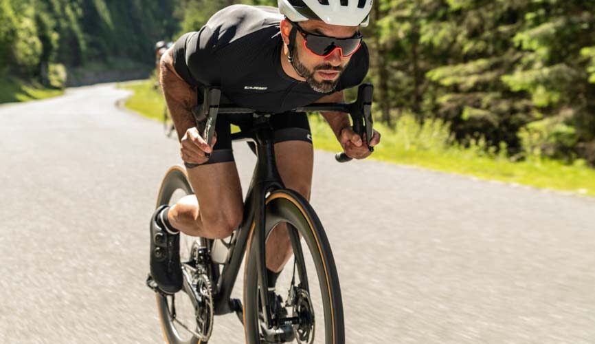 Man op een aero racefiets in diepe zithouding, met gestroomlijnde kleding en helm