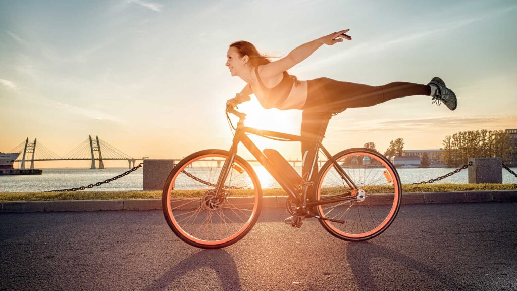Vrouw in sportkleding fietst blij, met één been gestrekt en de armen wijd – fietsen is gezond en geeft een gevoel van vrijheid. Vrouw in sportkleding fietst blij, met één been gestrekt en de armen wijd – fietsen is gezond en geeft een gevoel van vrijheid.
